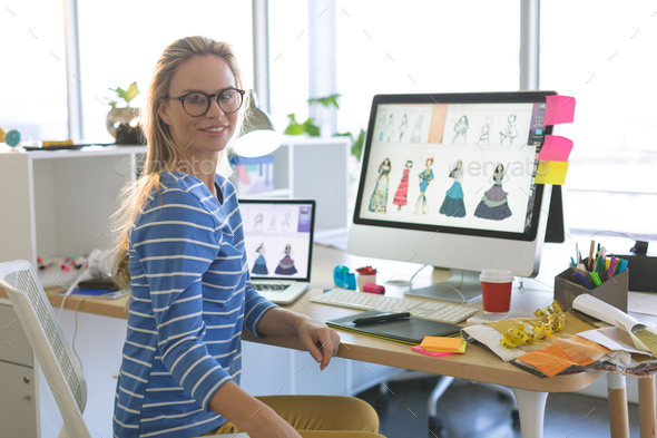 Female fashion designer looking at camera while sitting at desk in a modern office