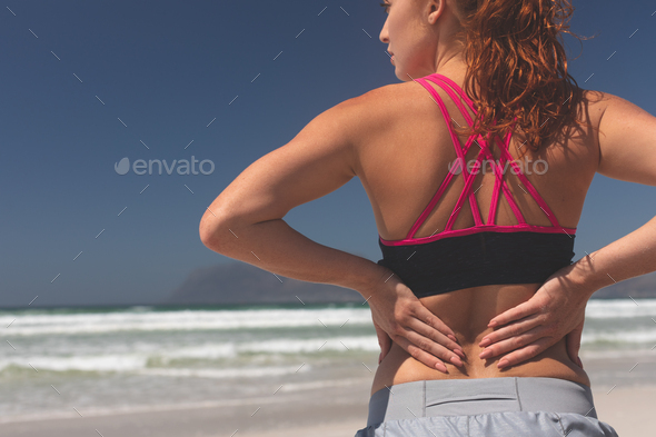 Fit woman standing with hand behind back at beach