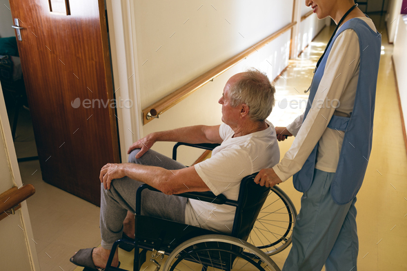 Female nurse pushing disabled senior male patient sitting in wheelchair at retirement home - Stock Photo - Images