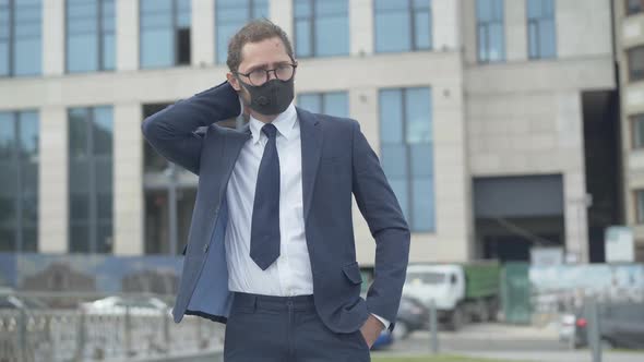 Portrait of Tired Caucasian Businessman in Eyeglasses and Face Mask Standing on Urban City Street alt