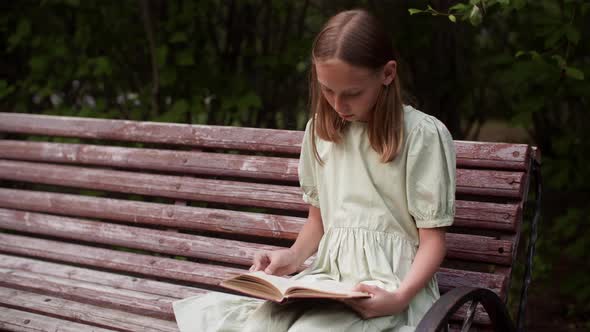 Teenager Girl Leafing Through Book Sitting on Park Bench at Summer Weekend alt