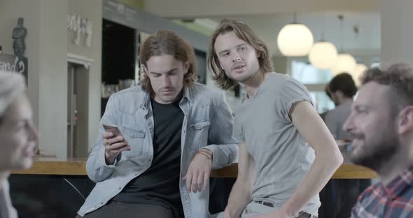 Man holding mobile phone and talking with another man in pub