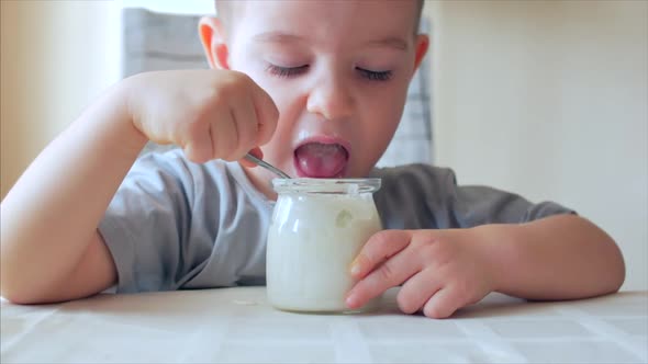 Close-up of a Baby Sitting at the Table and Eating Baby Food with a Spoon on Its Own. A 2-3 Year Old alt