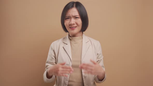 Asian business woman pointing herself and say who me, not me, isolated over beige background.