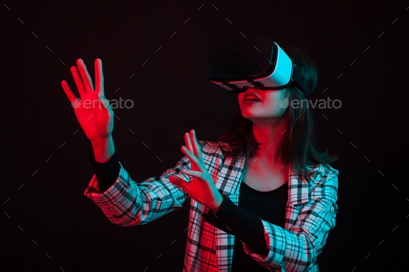 Beautiful young girl reaching out with her hands and wearing virtual reality goggles in studio with - Stock Photo - Images