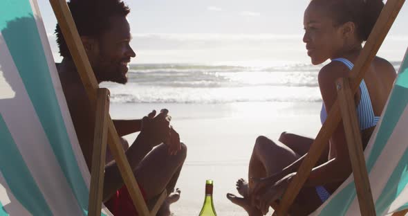 Portrait of african american couple smiling and sitting in deckchairs on the beach alt