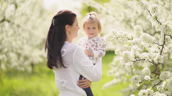 Mom Spinning with a Daughter in Her Arms in the Park By a Flowering Tree alt