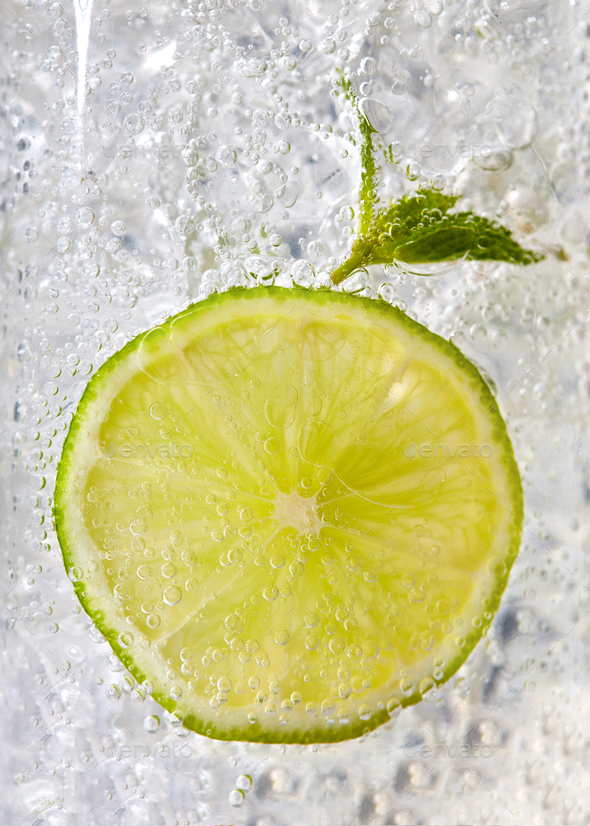 Macro photo of a piece of lime and mint leaf in a glass with ice and bubbles. Cold summer drink - Stock Photo - Images