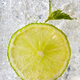 Macro photo of a piece of lime and mint leaf in a glass with ice and bubbles. Cold summer drink - PhotoDune Item for Sale