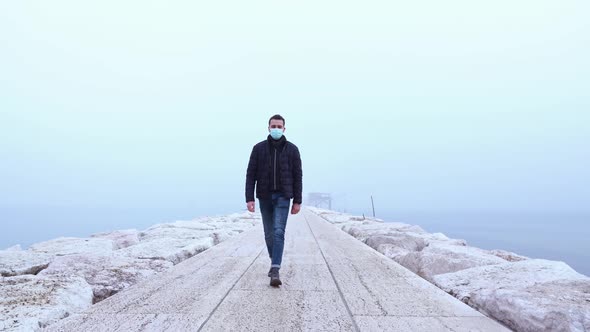 Young Tall Man Wearing Protective Mask Walks on Sea Pier alt