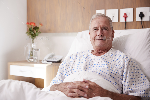 Portrait Of Male Senior Patient Lying In Hospital Bed Smiling At Camera ...