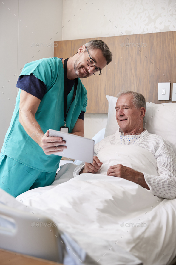 Surgeon With Digital Tablet Visiting Senior Male Patient In Hospital Bed In Geriatric Unit