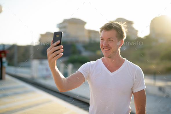 Happy man taking selfie with mobile phone at train station