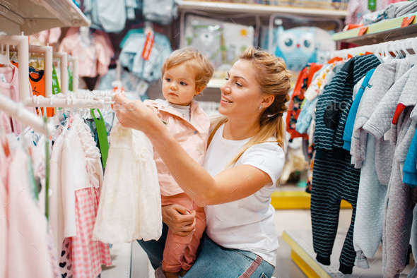 Mother with girl choosing clothes in kids store
