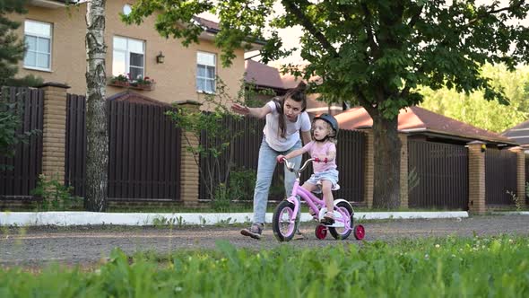 mother teaches her daughter to ride a bike. Little girl in helmet learns to ride alt