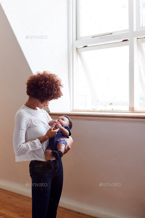 Loving Mother Holding Sleeping Newborn Baby By Window At Home In Loft Apartment