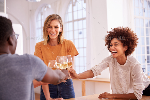 Two Couples Relaxing In Kitchen At Home Making A Toast With Glass Of Wine Together