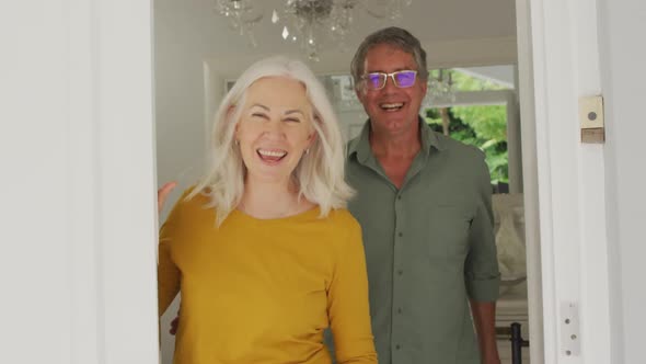 Animation of happy caucasian senior couple opening doors and welcoming friends alt