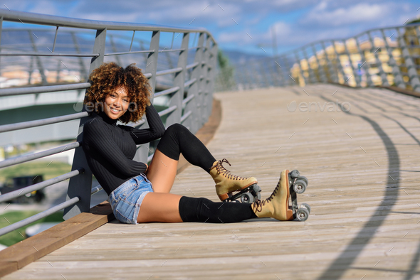 Afro hairstyle woman on roller skates sitting on urban bridge - Stock Photo - Images