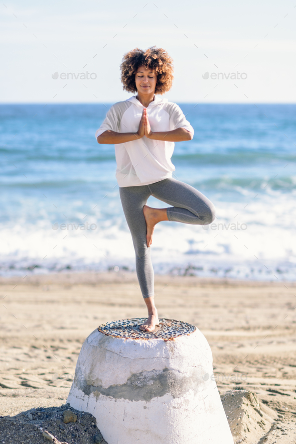 Young black woman doing yoga in the beach.