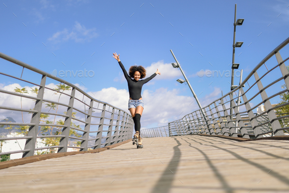 Afro hairstyle woman on roller skates riding outdoors on urban bridge - Stock Photo - Images