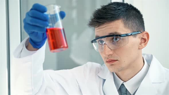 Scientist Looking At Flask With Red Liquid