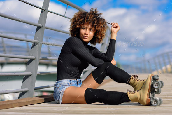 Afro hairstyle woman on roller skates sitting on urban bridge - Stock Photo - Images