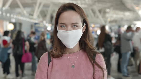 Portrait of a Woman in Medical Mask Looking Straight at Camera in Airport Terminal Preventing alt