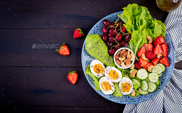 Plate with a paleo diet food. Boiled eggs, avocado, cucumber, nuts, cherry and strawberries