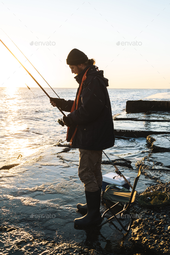 Man fisherman wearing coat standing with a fishing rod