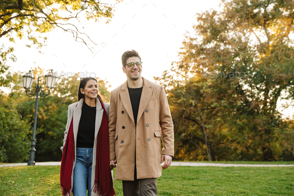 Portrait of young casual couple smiling at camera and walking in autumn park