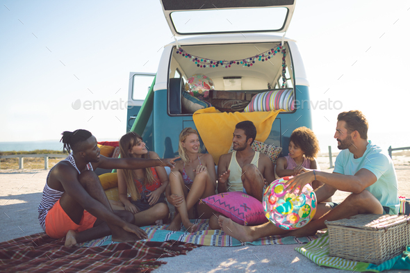 Front view of group of diverse friends interacting with each other near camper van at beach