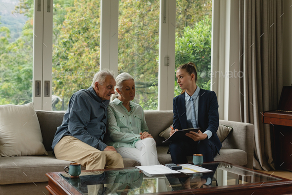Active senior Caucasian couple discussing with real estate agent over documents in living room