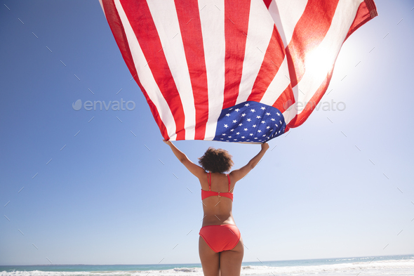 Low angle view of African american woman in bikini holding american flag on the beach