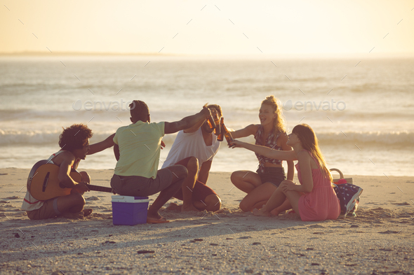 Front view of happy group of diverse friends toasting beer bottles on the beach