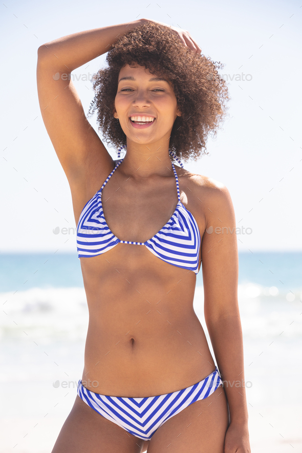 Front View Of Beautiful Happy Mixed Race Woman In Bikini Looking At Camera On The Beach Stock