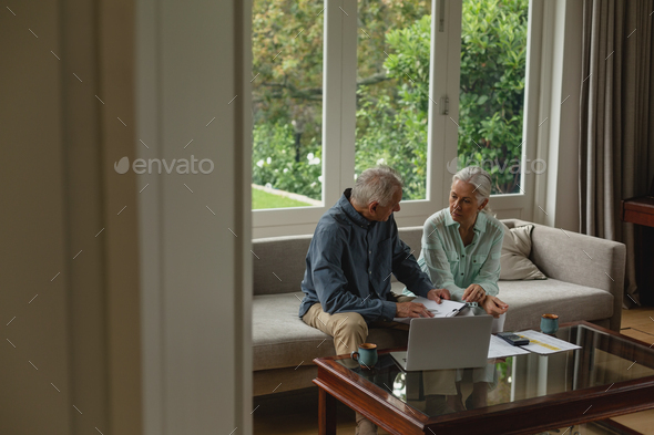 Side view of active senior Caucasian couple calculating bills in living room at home