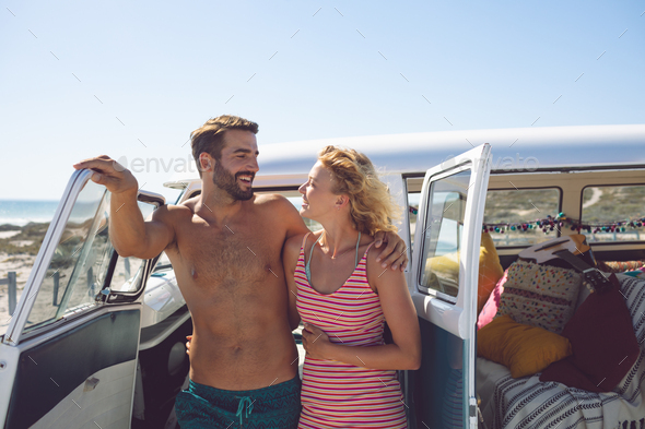 Happy Caucasian couple talking with each other near camper van at beach in the sunshine