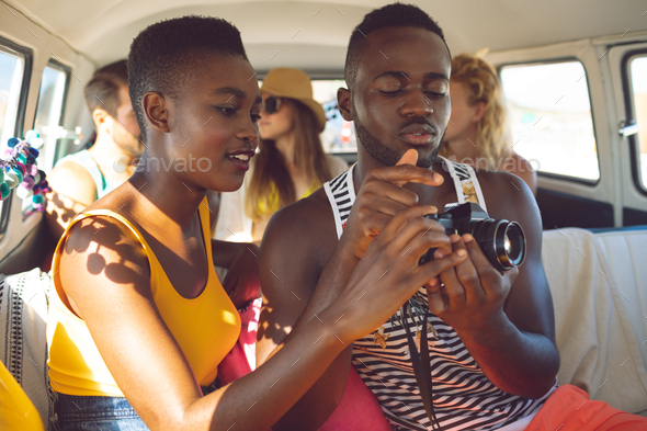 Young African american friends reviewing photos on digital camera in camper van at beach.