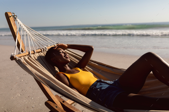 Side view of young African-american woman relaxing in a hammock on the beach