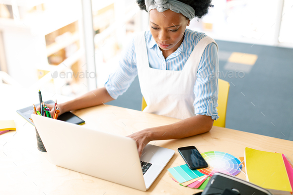 African american female graphic designer using graphic tablet and laptop at desk in office