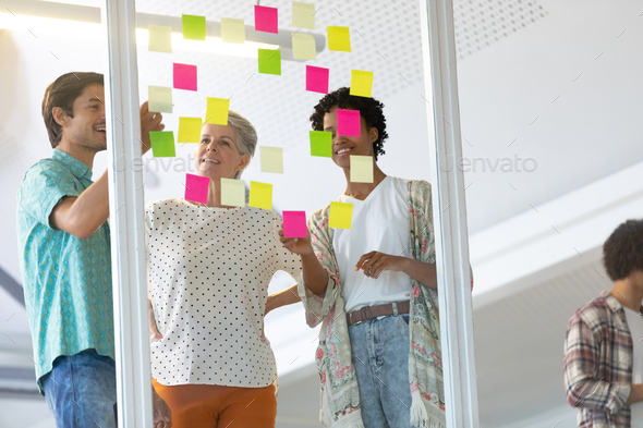 Front view of diverse business people discussing over sticky notes in the modern office