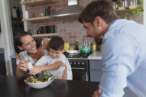 Side view of happy Caucasian family preparing vegetable salad in kitchen at home
