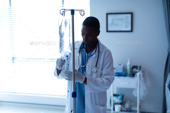 Front view of African-american male doctor checking intravenous therapy drip in the ward at hospital