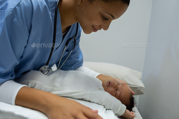 Mixed-race female doctor examining baby with stethoscope on table of medical examination room