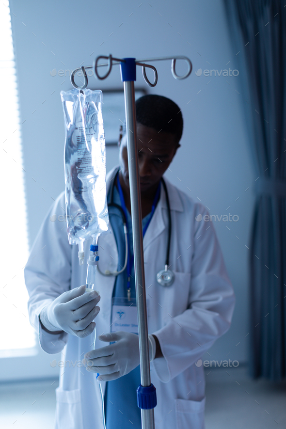 Front view of African-american male doctor checking intravenous therapy drip in the ward at hospital