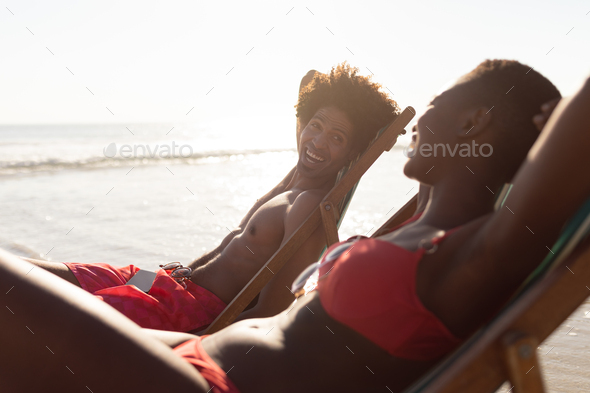 Happy African-american couple interacting with each other while relaxing in a beach chair