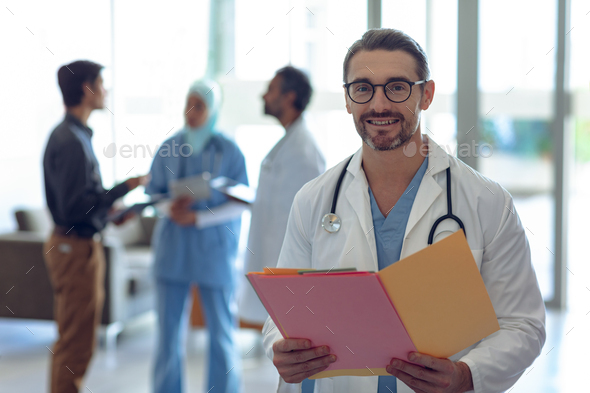 Happy Caucasian male doctor holding medical file and looking at camera in hospital.