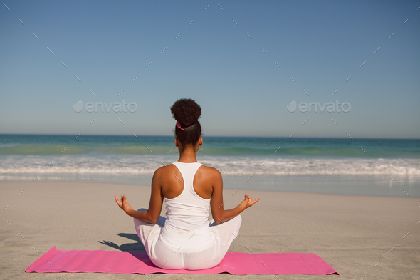 Rear view of African american woman doing yoga on exercise mat at beach in  the sunshine Stock Photo by Wavebreakmedia