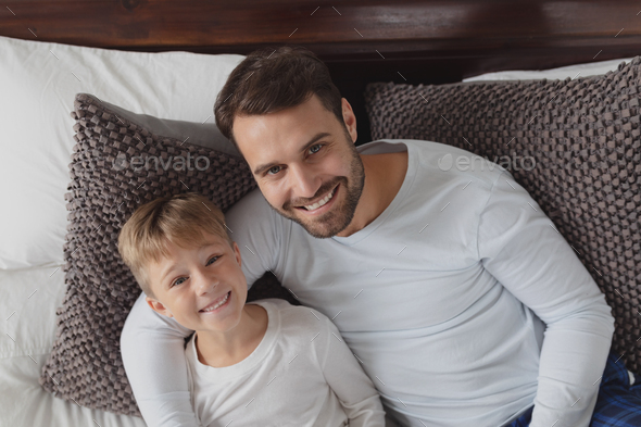 Caucasian father and son looking at camera while lying on bed